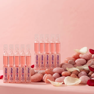 Nine Vitd-ss Puren Serum 1.5ml ampoules arranged on a pink surface with decorative stones and petals against a soft pink background.